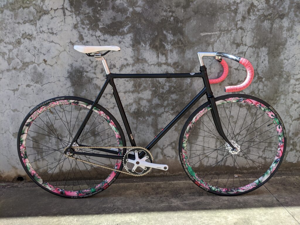 Black 56 cm Medium/Large Fixie Road Bike with Velocity wheels. The floral pattern rims & pink bartape highlight the black frame